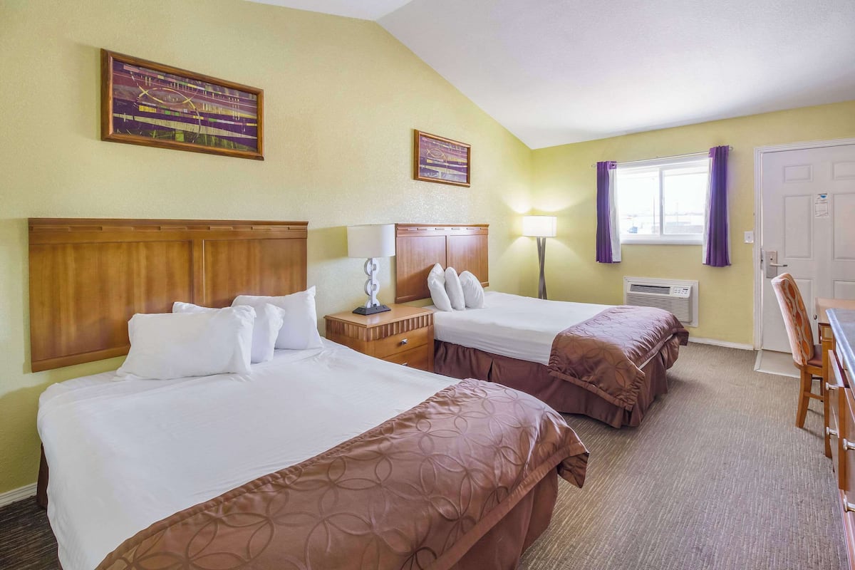 A hotel room with two beds, a desk, a chair, a lamp, and a window with purple curtains.