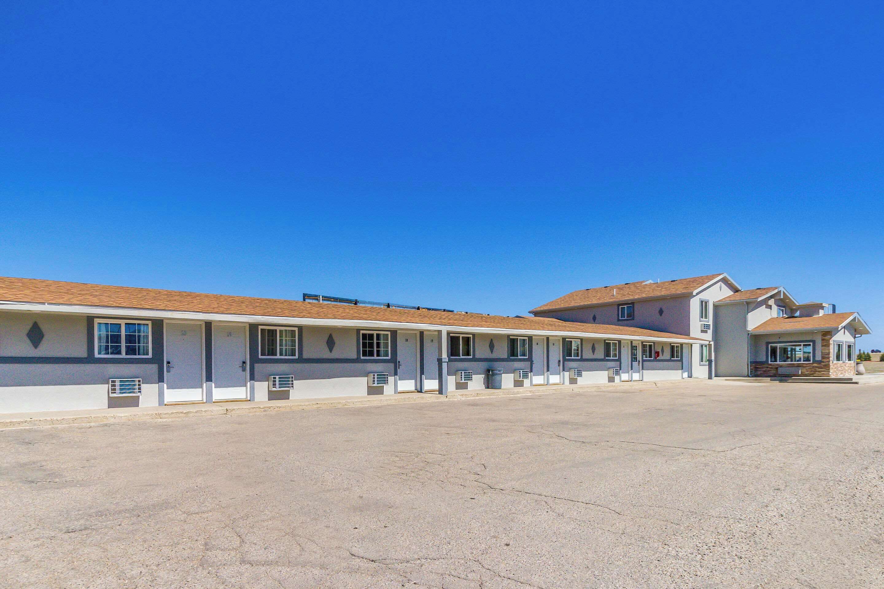 Una fila di edifici in stile motel con camere individuali, un parcheggio e un cielo azzurro intenso.