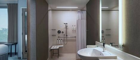 A modern hotel bathroom with a shower, a sink, and a large mirror.