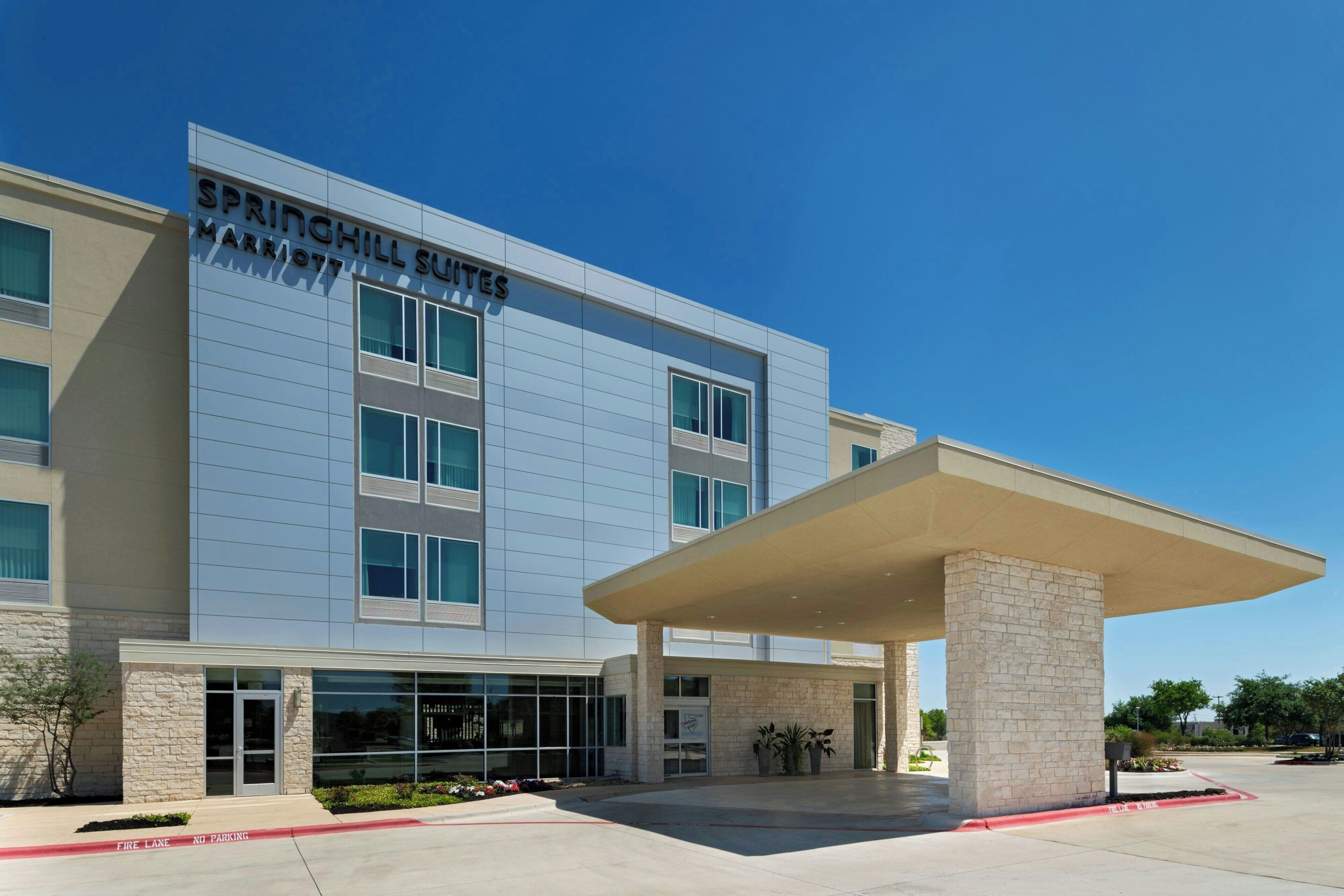 A modern hotel with a flat facade, large windows, and a covered entrance area.