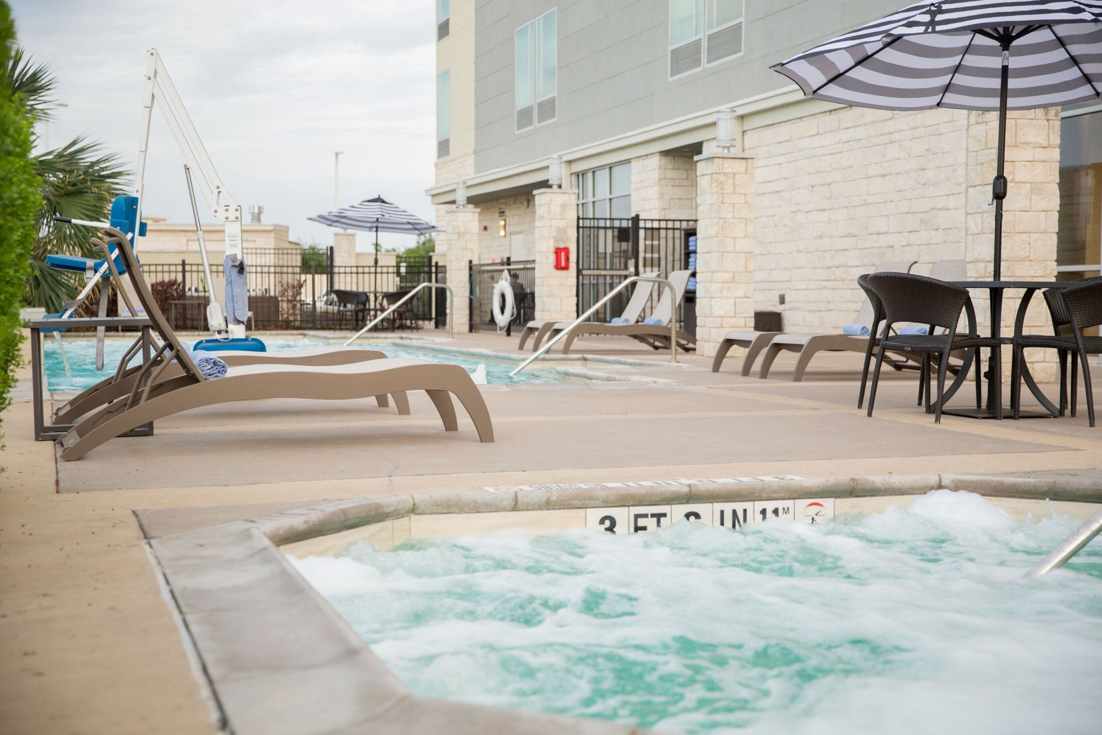 A pool area with lounge chairs, a hot tub, and a table with chairs.