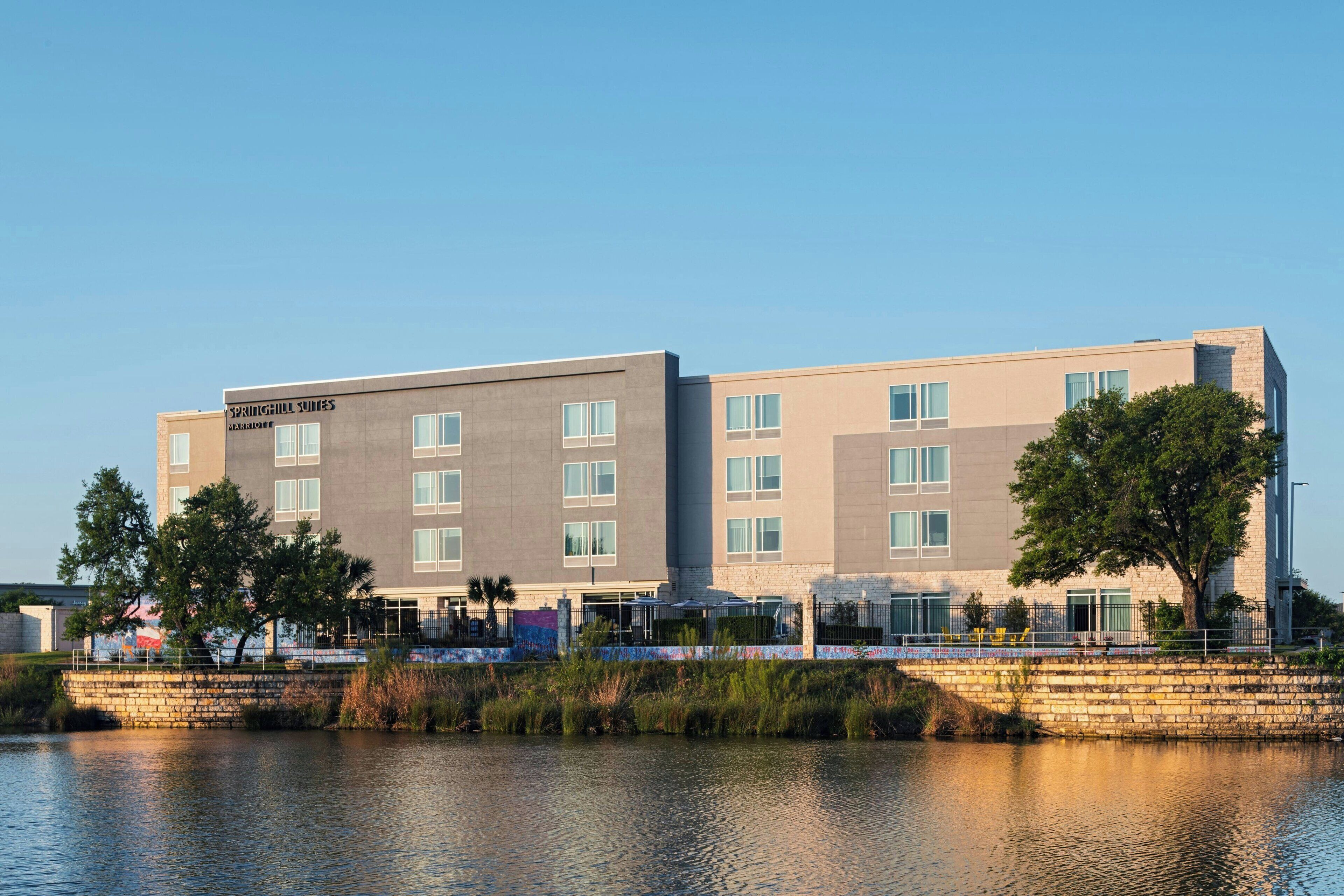 A modern hotel with a flat roof, multiple windows, and a stone bridge in front.