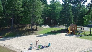 A sandy beach area with a wooden deck, a swing set, and a small playhouse.