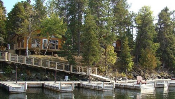 A cabin with a dock extending into a lake, surrounded by dense forest.