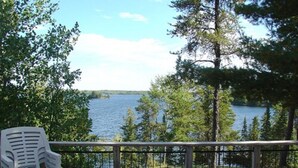 A deck with a view of a lake, a picnic table, and a white plastic chair.