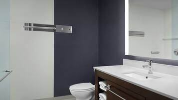 A modern bathroom with a white toilet, a dark wall, a white sink with a mirror above it, and a towel rack.