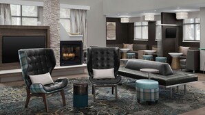 A modern living room with a fireplace, leather armchairs, a sofa, and ottomans. - Residence Inn by Marriott Jacksonville South/Bartram Park (Jacksonville)
