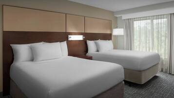A hotel room with two beds, a headboard with storage compartments, a bedside table, and a window with curtains.