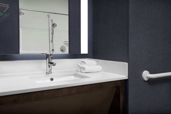 Un baño con lavamanos blanco, espejo y toallero.