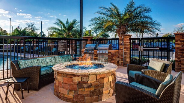 An outdoor patio area with a stone fire pit, wicker furniture, and a grill. - Residence Inn by Marriott Jacksonville South/Bartram Park (Jacksonville)