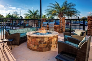 Un patio al aire libre con un hogar a leña de piedra, muebles de mimbre y una parrilla.