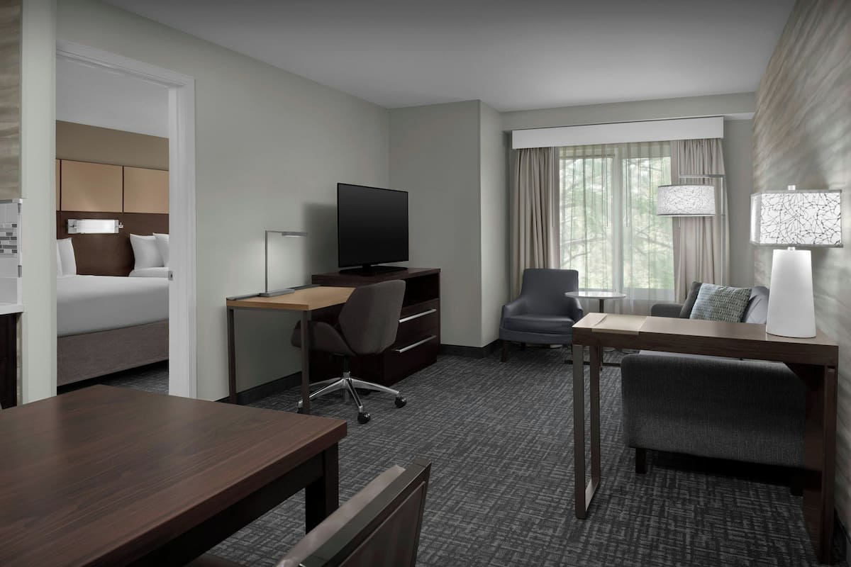 Une chambre d’hôtel comprenant un lit, un bureau avec une télévision, une chaise, une petite table et une fenêtre avec des rideaux.