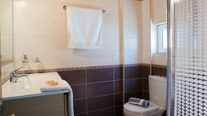 Un baño con lavamanos, espejo, toallero, inodoro y zona de ducha.