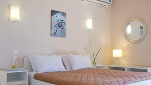 Habitación de hotel con cama, mesitas de noche, aire acondicionado de pared, un cuadro de bicicleta y un espejo redondo.