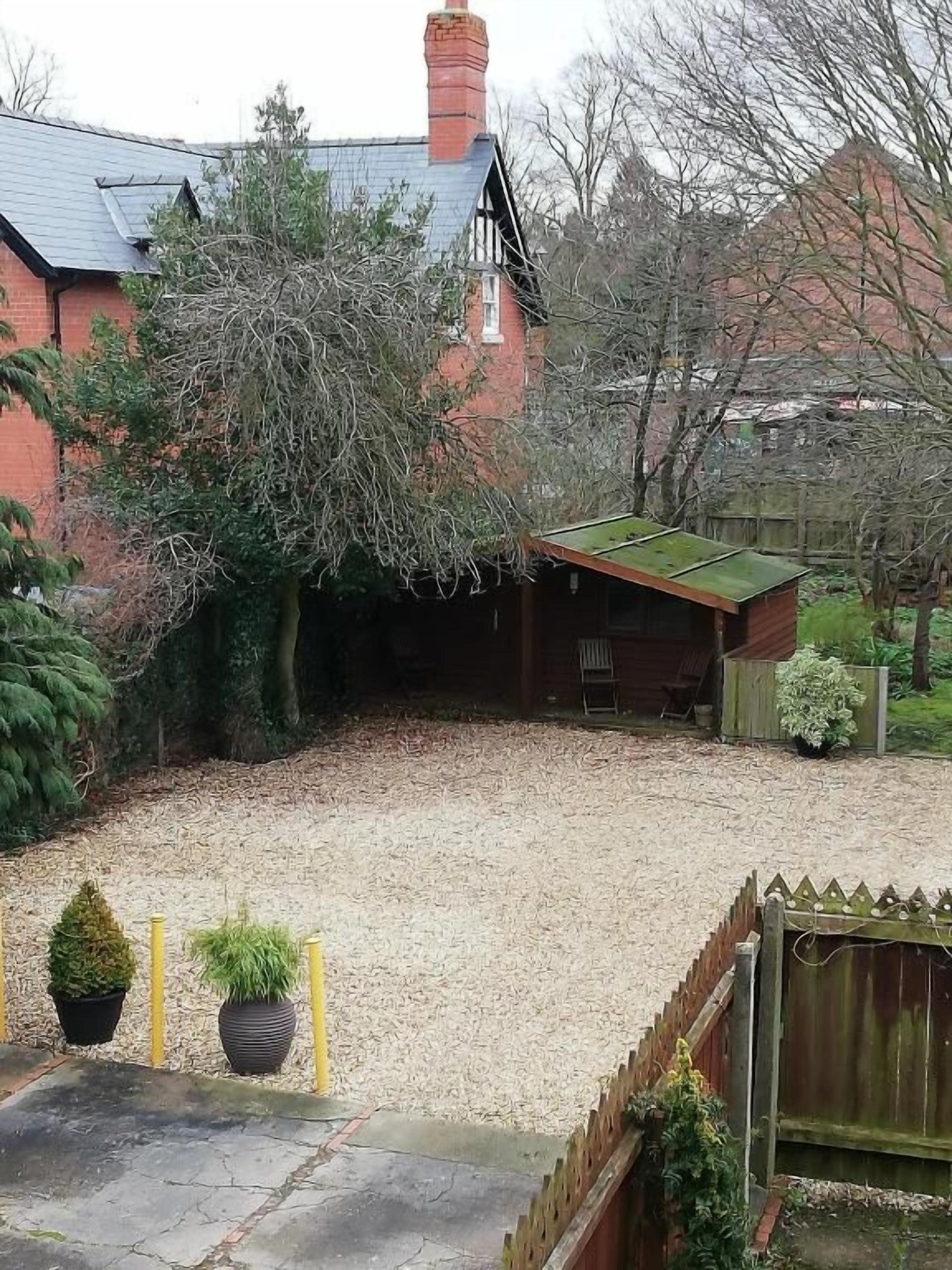 A residential property with a gravel driveway, a wooden fence, and a brick house with a green roof.