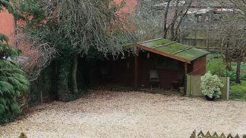 A residential property with a gravel driveway, a wooden fence, and a brick house with a green roof.