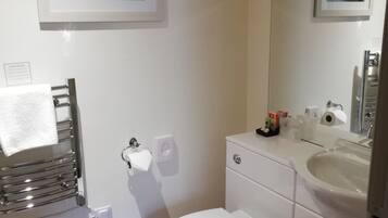 Ein kleines Badezimmer mit Toilette, Waschbecken und Handtuchhalter. Darüber hängt ein gerahmtes Bild an der Wand.