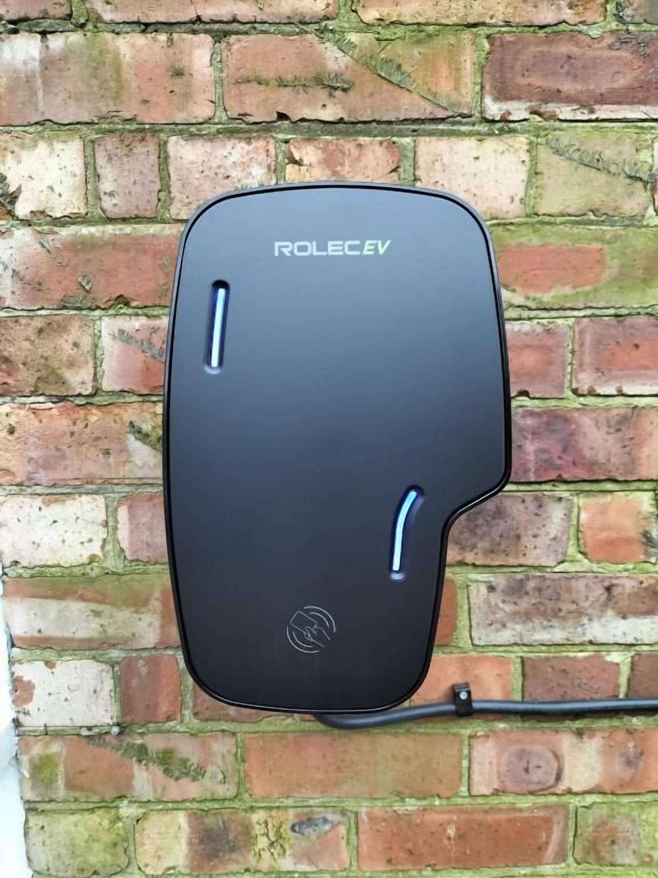 A black electronic device, possibly a charging station, mounted on a brick wall.