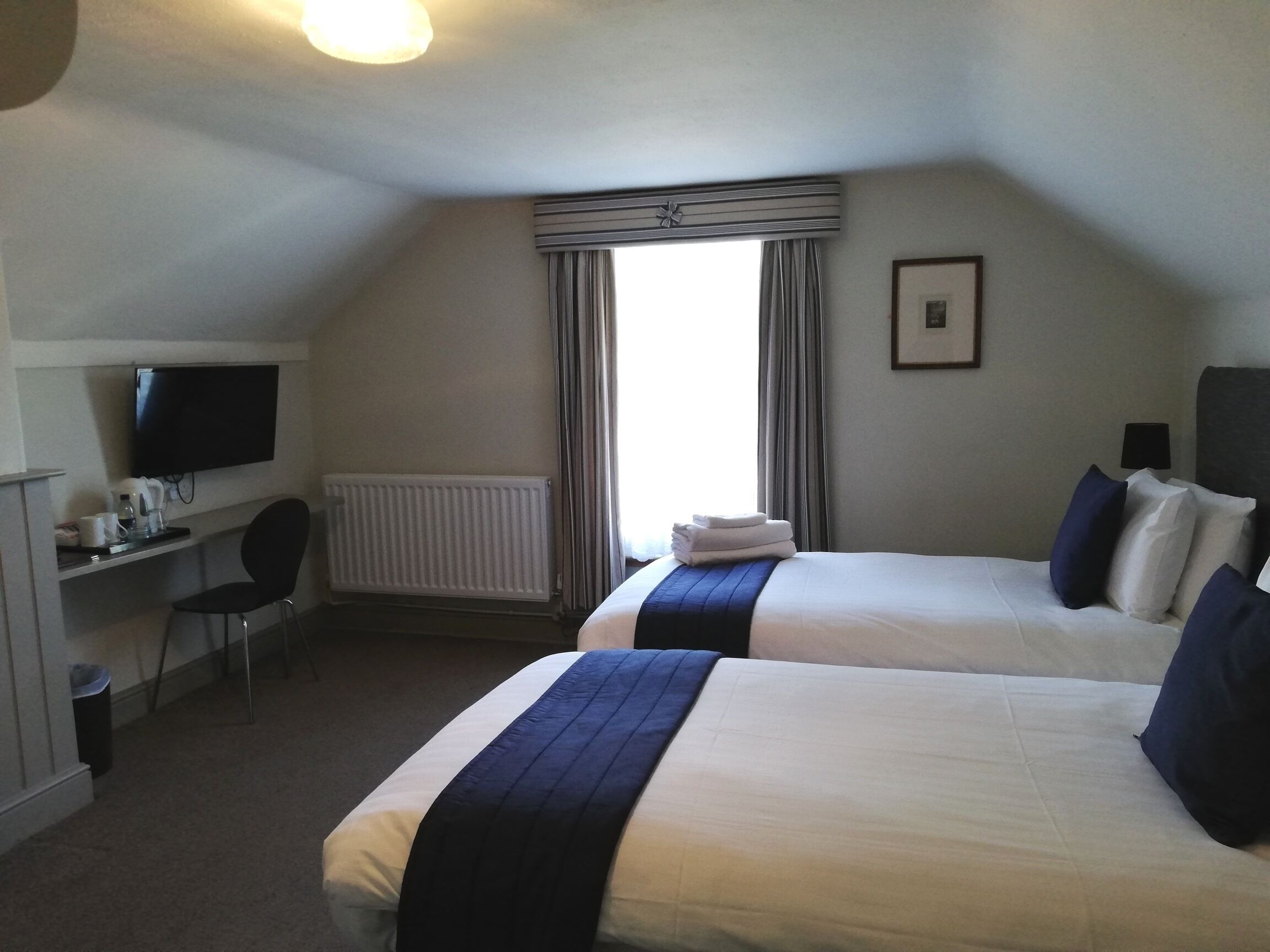 A hotel room with two beds, a desk with a chair, a television, and a window with curtains.