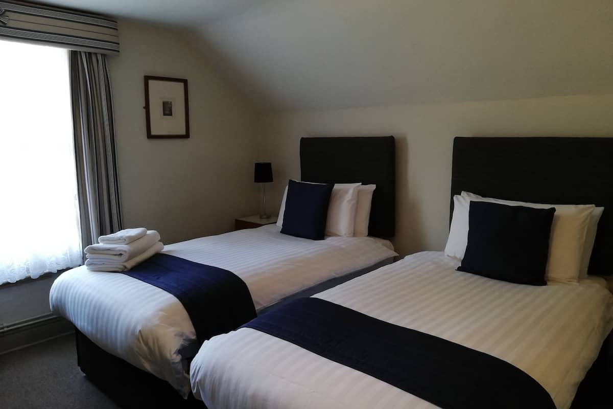 A hotel room with two beds, a nightstand with a lamp, a framed picture on the wall, and a window with curtains.
