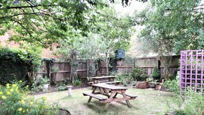 Un patio trasero con una mesa de picnic de madera rodeado de un jardín con diversas plantas y una cerca de madera.