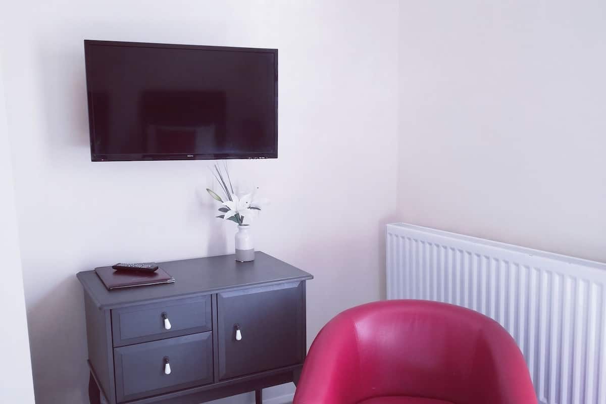A room with a dark wooden cabinet, a red armchair, a flat-screen TV mounted on the wall, and a radiator.