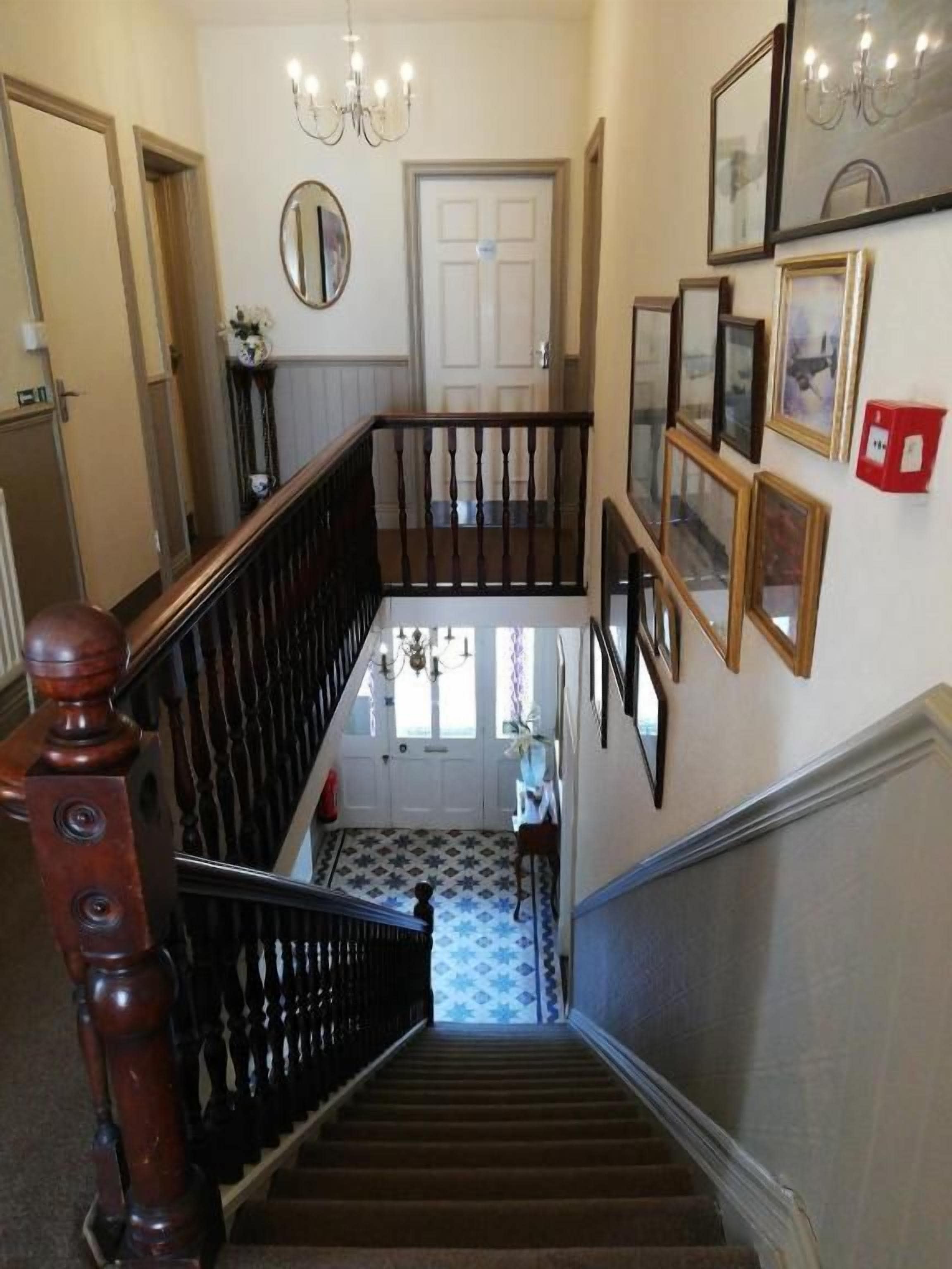 A staircase with a wooden handrail and a glass railing, leading to a room with a patterned floor.
