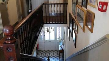 A staircase with a wooden handrail and a glass railing, leading to a room with a patterned floor.