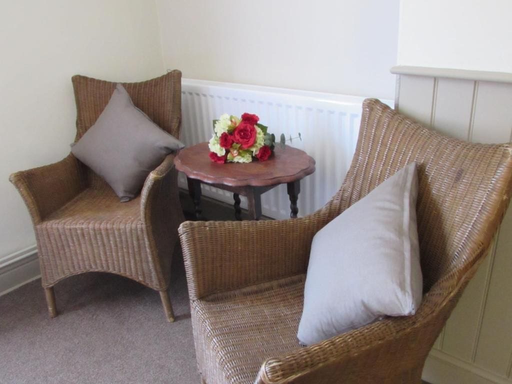 Una habitación con dos sillones de mimbre y una mesita con un ramo de flores.