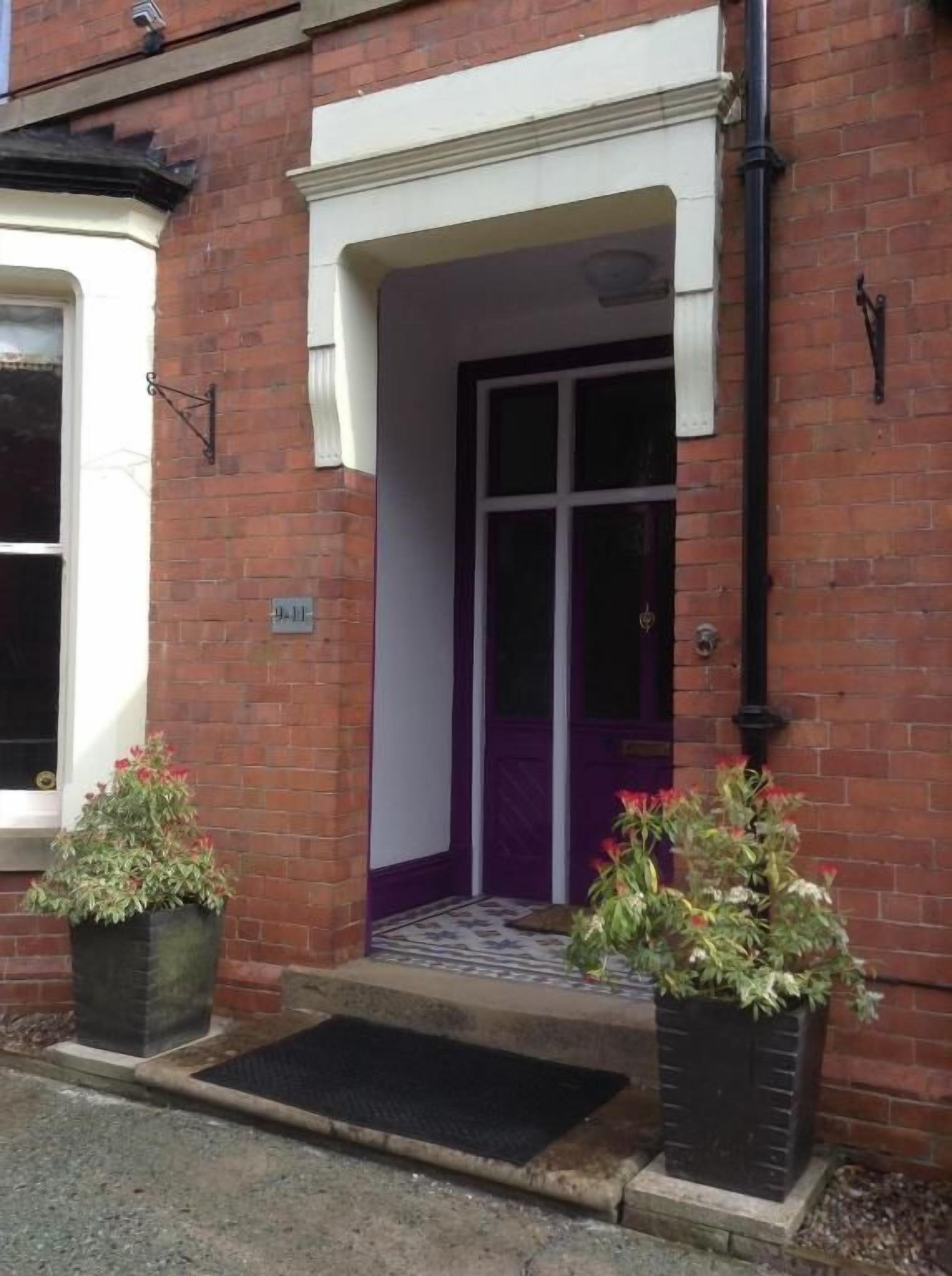 A building entrance with a purple door, a brick facade, and two potted plants.