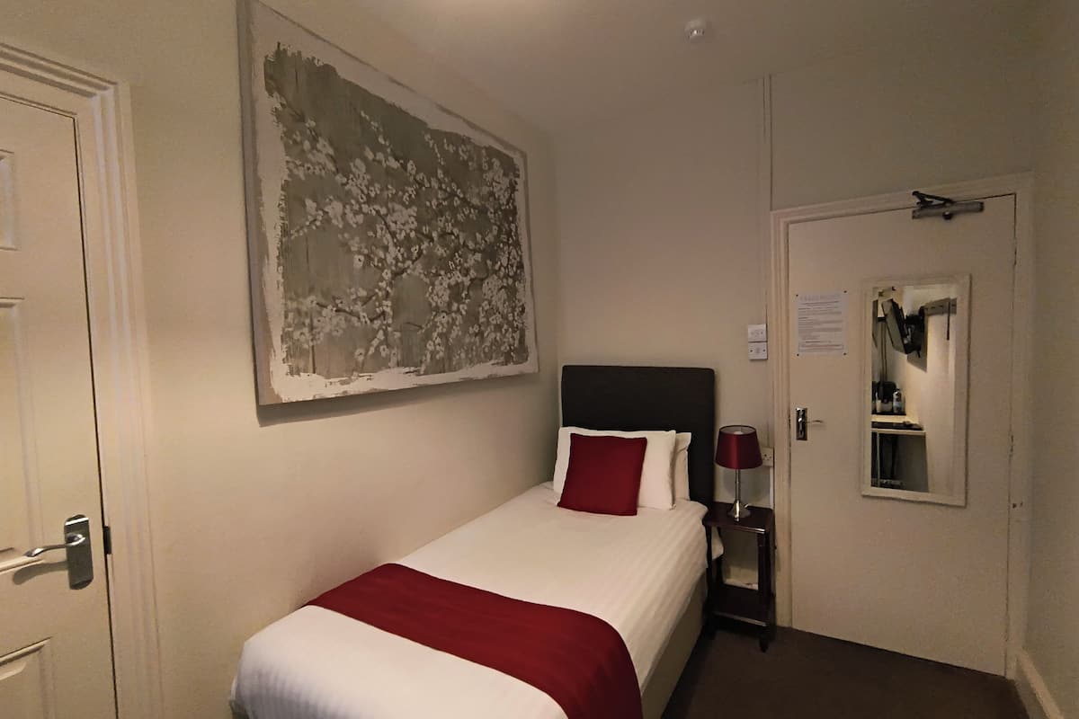 A hotel room with a bed, a nightstand, a lamp, a painting, and a door.