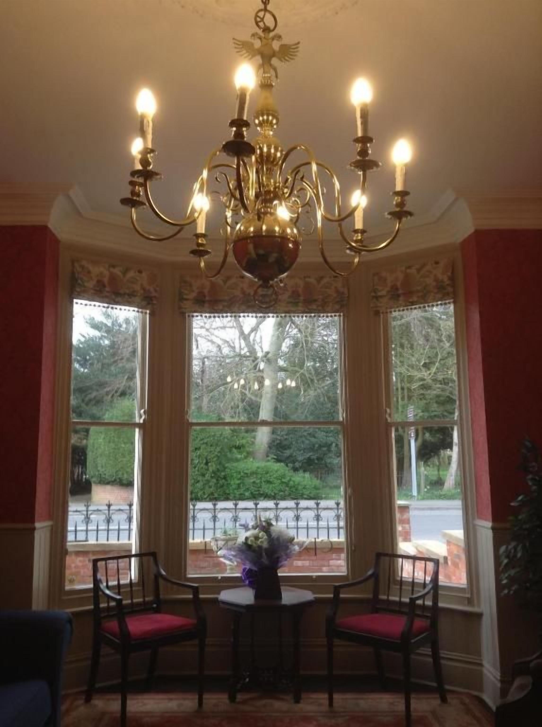 A room with a chandelier, two chairs, a table, and large windows with a view of greenery.