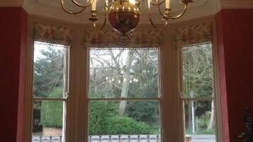 A room with a chandelier, two chairs, a table, and large windows with a view of greenery.
