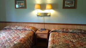 Quarto de hotel com duas camas, cada uma com colcha acolchoada, uma mesa de cabeceira no meio e duas luminárias fixadas na parede.