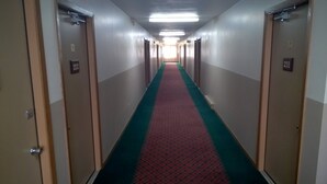 Corredor de hotel com portas numeradas 212 e 211, com carpete em vermelho e verde, e uma lâmpada fluorescente no teto.