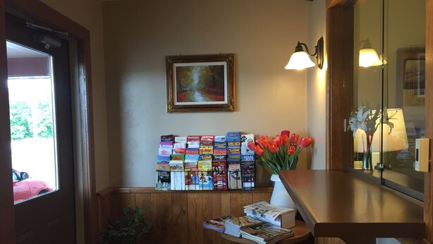 Uma área de recepção com um banco de madeira, um porta-revistas fixado na parede, um vaso com tulipas vermelhas e um quadro emoldurado.