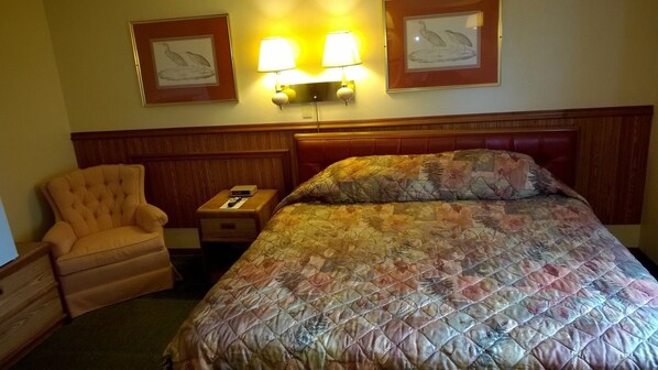 Une chambre d’hôtel comprenant un lit, une chaise, une table de chevet et deux lampes fixées au mur.