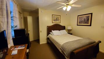Een hotelkamer met een bed, een bureau, een stoel, een plafondventilator en twee schilderijen aan de muur.