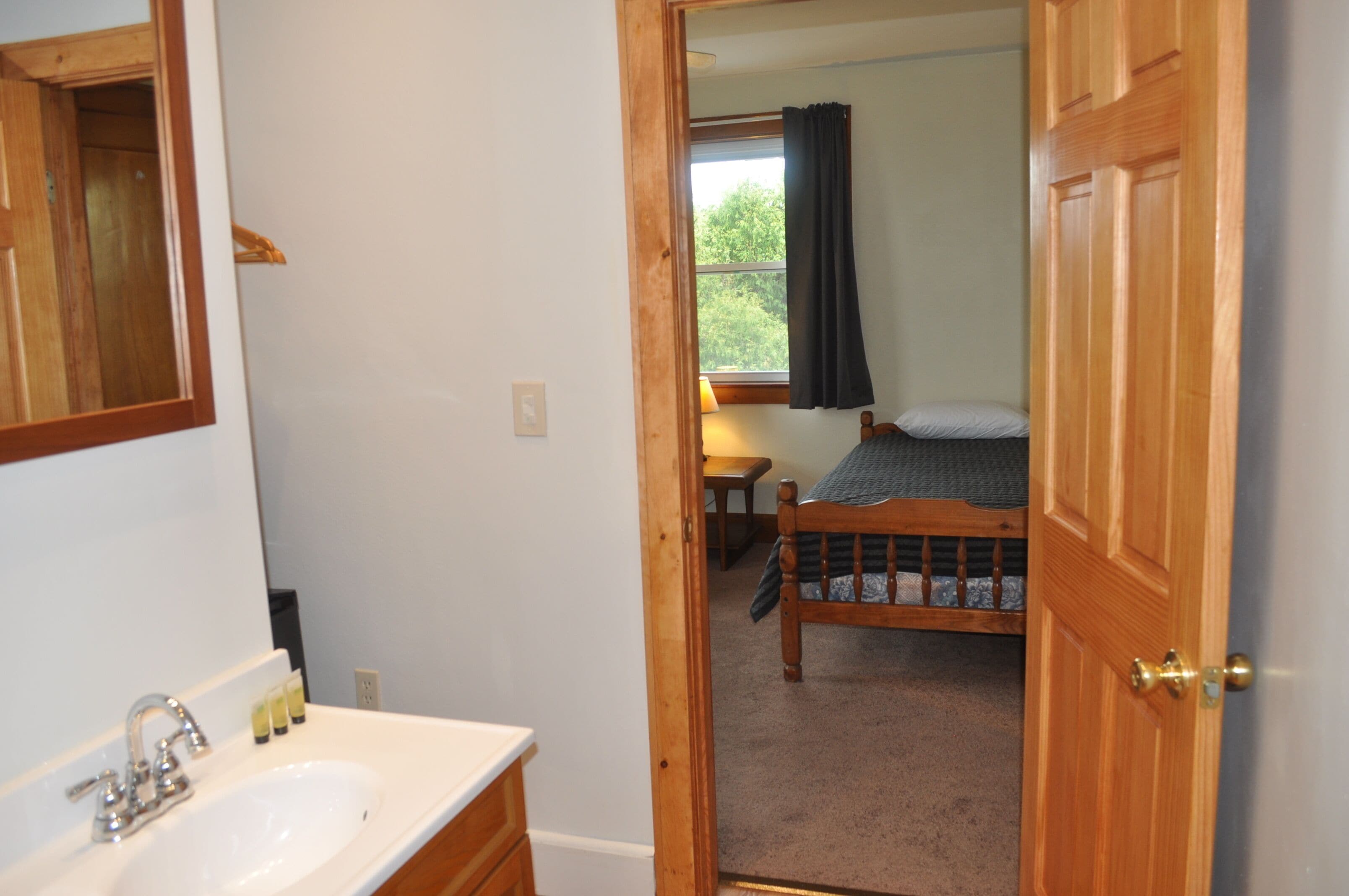 A bedroom with a wooden bed, a bedside table, and a window with a curtain.
