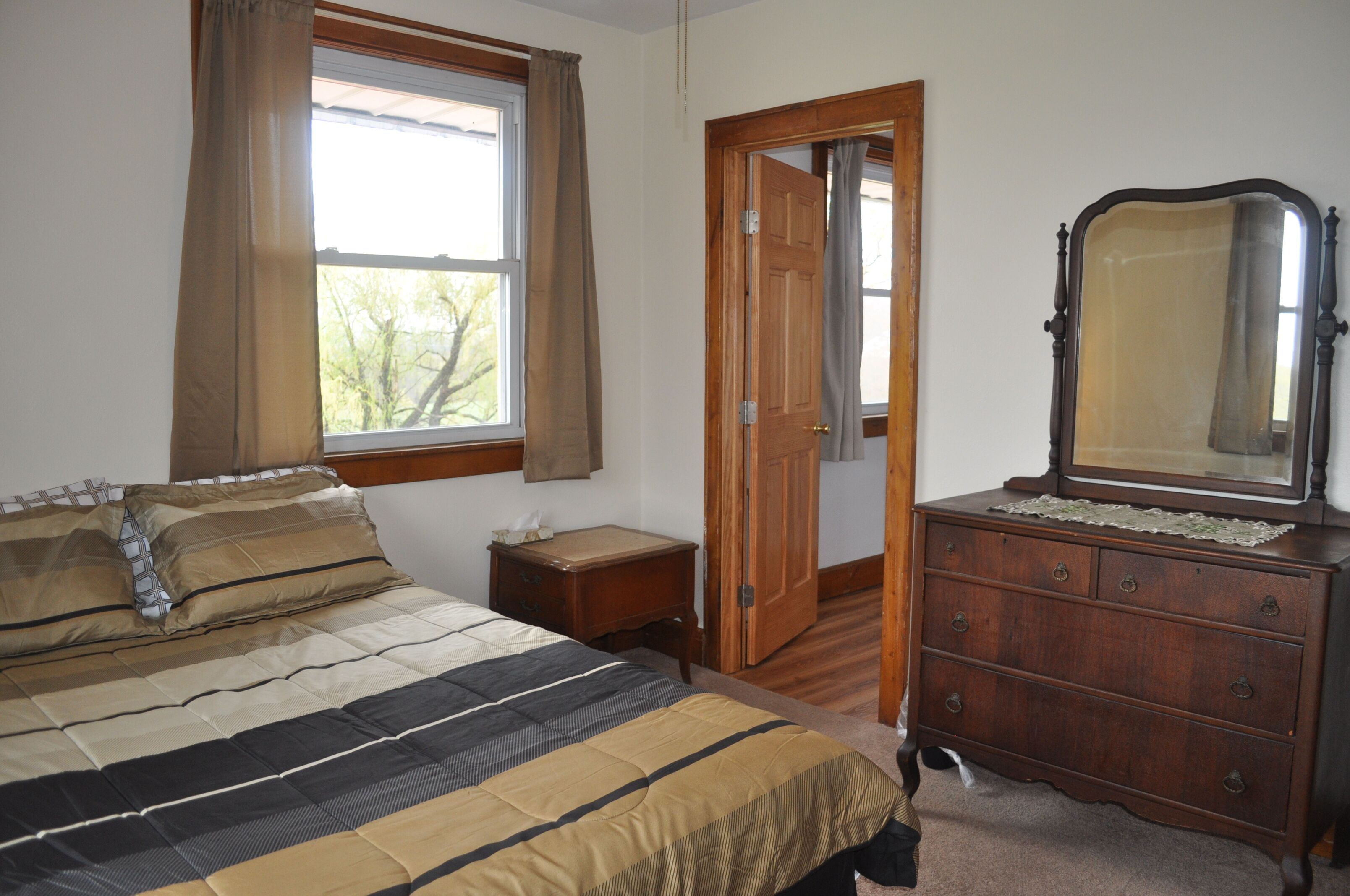 A bedroom with a bed, a dresser, a mirror, and a window with curtains.