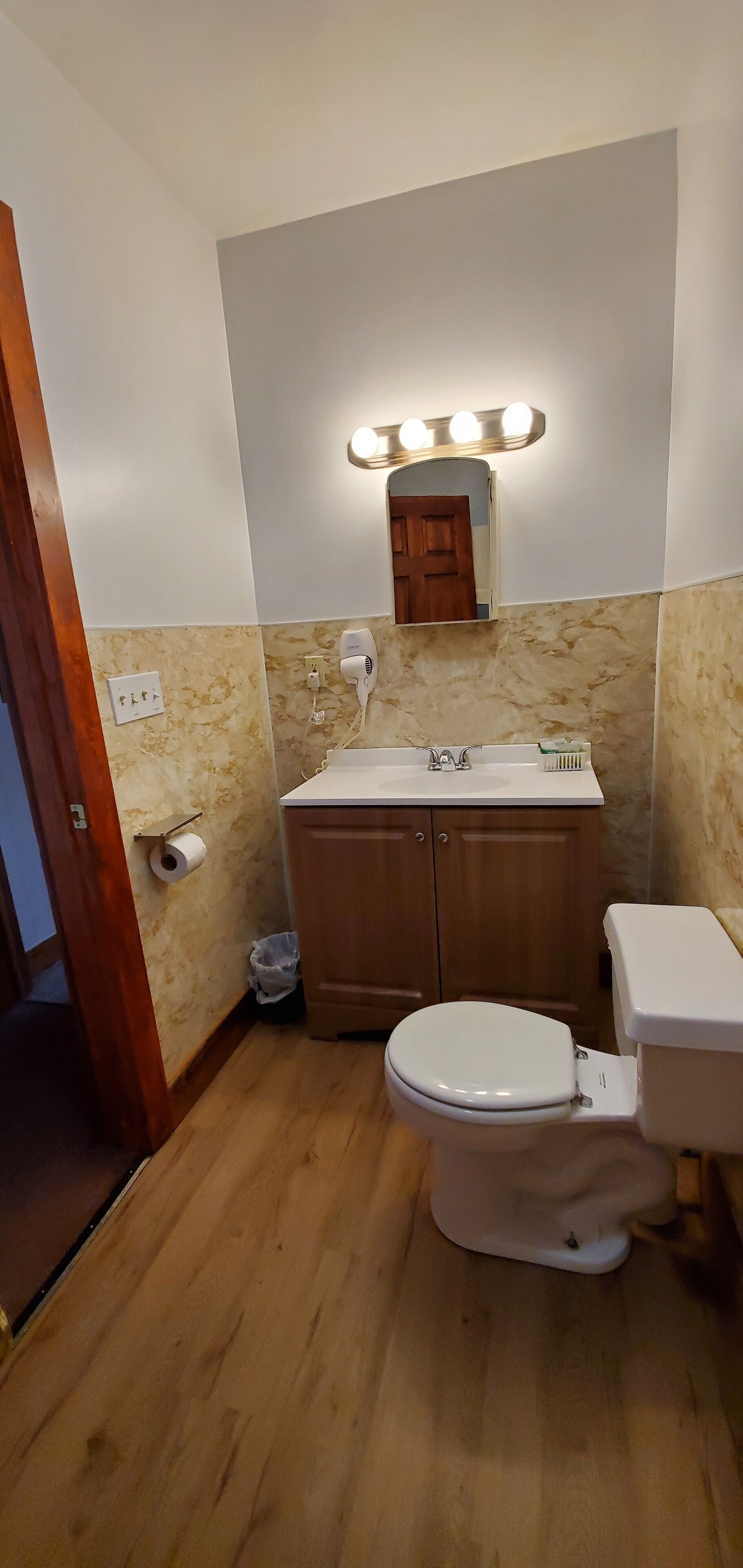 Un baño con inodoro, lavamanos, tocador y espejo con iluminación.
