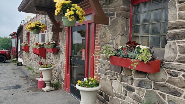 Un edificio de piedra con marcos rojos en ventanas y puertas, macetas con flores en el exterior y una cesta colgante con flores.