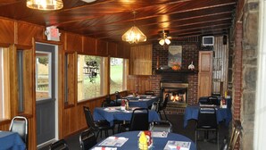 Un restaurante con paredes de madera y chimenea de ladrillo. Las mesas están dispuestas con manteles azules y ofrecen menús.
