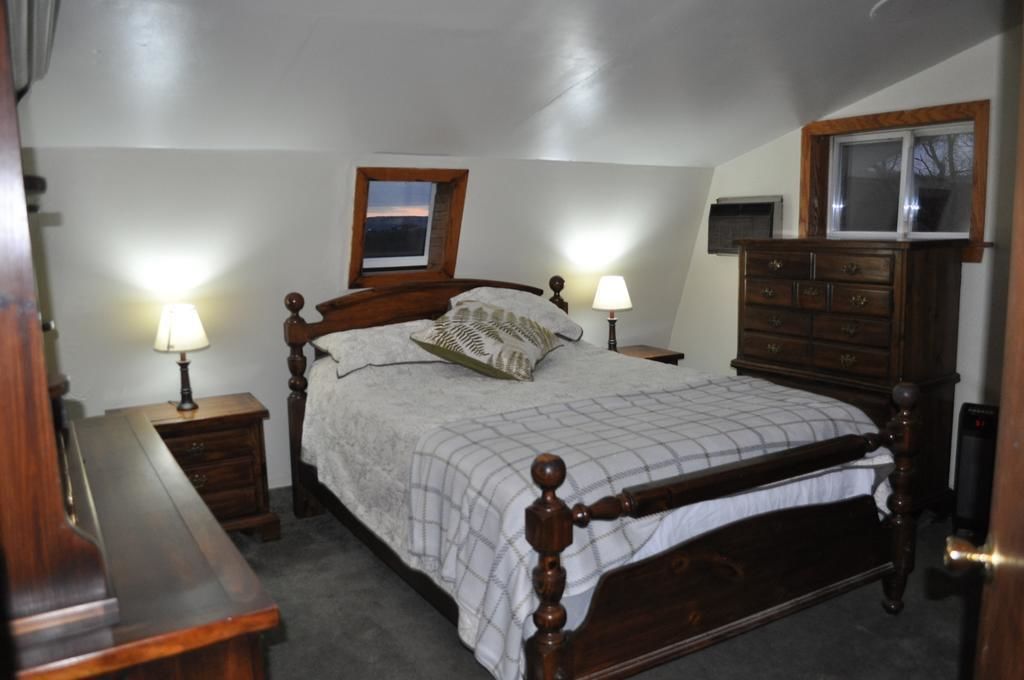 Une chambre à coucher avec un lit en bois, deux tables de chevet avec des lampes, une commode et une fenêtre donnant sur un beau paysage.