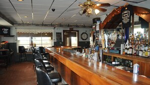 Un bar con mostrador de madera, taburetes y una variedad de botellas y vasos.