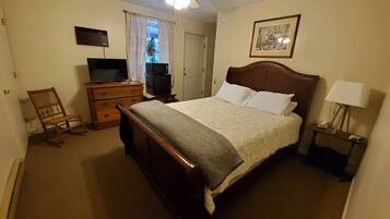 Quarto com cama de madeira, ventilador de teto, televisão, cômoda e abajur.