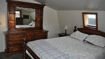 Un dormitorio con cama de madera con dosel, cómoda con varios cajones, mesita de noche con lámpara y ventana con vistas.