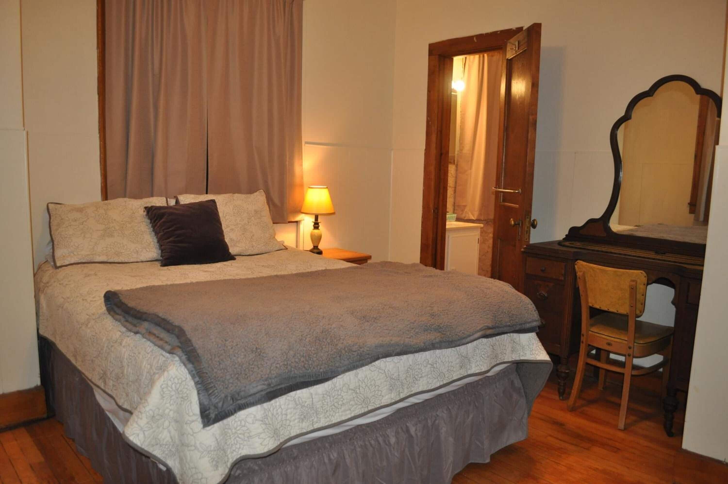 Une chambre à coucher avec un grand lit, un bureau en bois, une chaise, une lampe et un miroir.