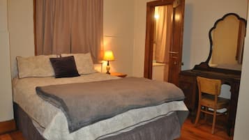 Une chambre à coucher avec un grand lit, un bureau en bois, une chaise, une lampe et un miroir.