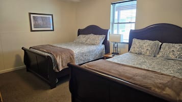 Habitación de hotel con dos camas, una mesita de noche, una lámpara, un cuadro en la pared y una ventana con persianas.
